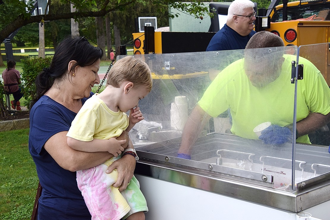 Visiting her grandson from Long Island, Stacy Hoffman hoists Windingwood Road resident Levi Rubin for a better view of the ice cream scooped by Paul Vinci, a Rye Brook Highway Department employee.