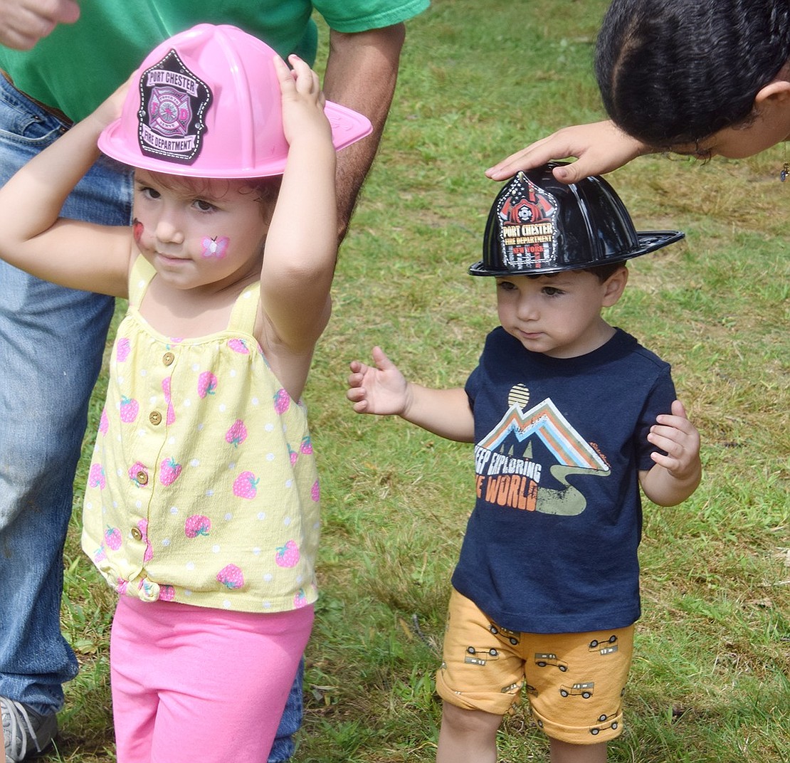 Charlee and Lenox Diaz, ages 3 and 2, of Francis Lane, struggle to keep the plastic Port Chester Fire Department hats they received from the Port Chester volunteer firefighters on hand at the park on their heads.