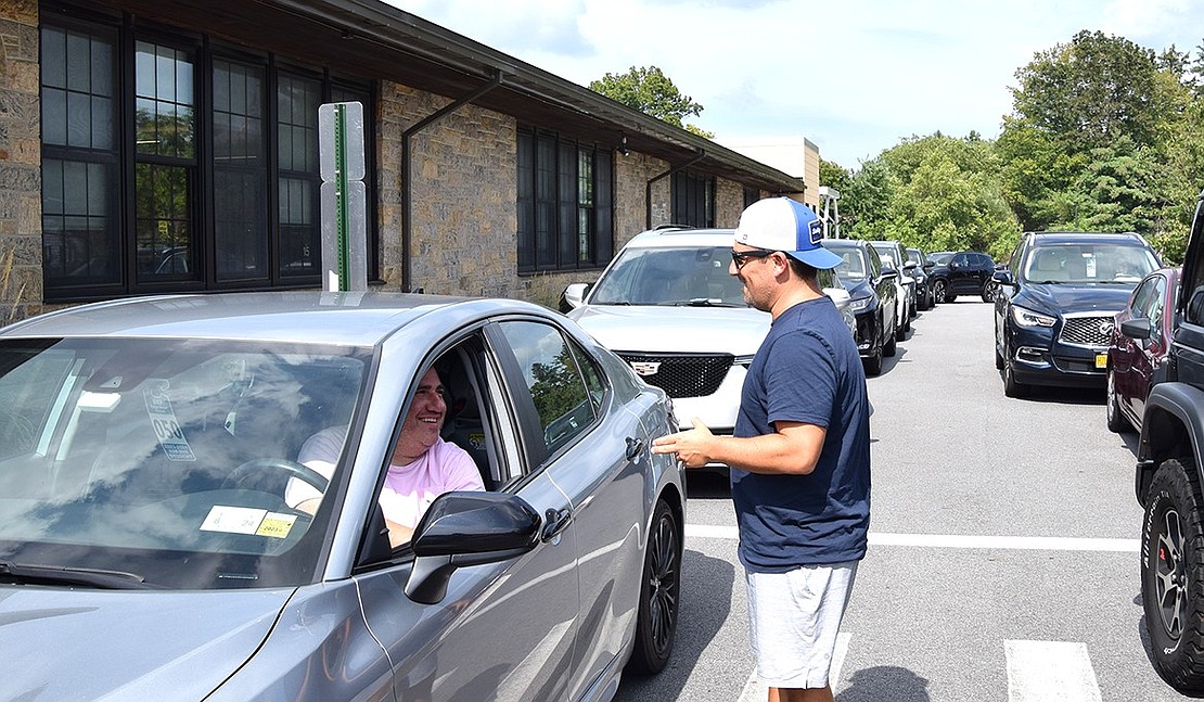 Eric Hammer (left) and Ed Teig (right) make small talk while waiting for students to be let out of Ridge Street Elementary School for dismissal. Behind them, parents wait in their cars trying to beat the 90-degree heat.