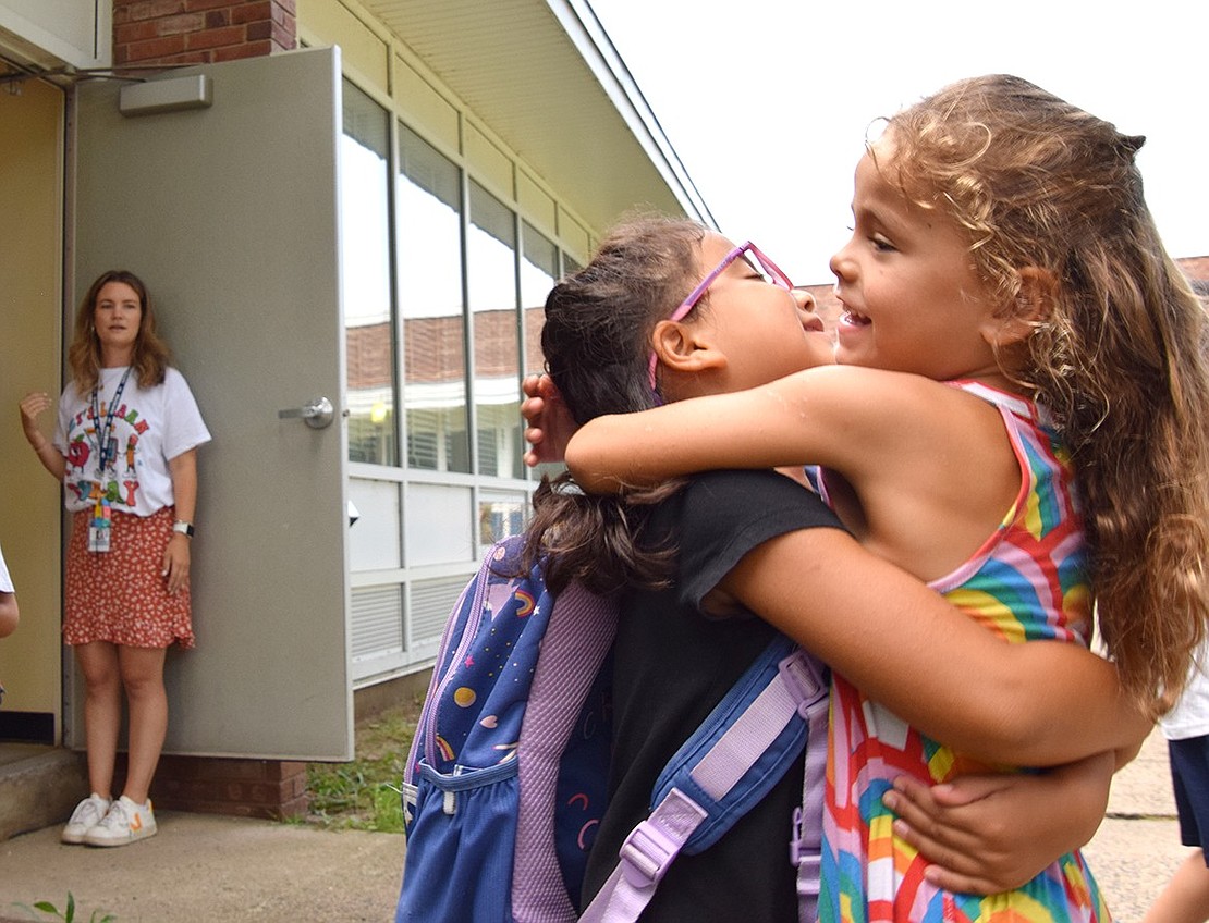 Hyped up during dismissal after her second day of classes at King Street Elementary School on Friday, Sept. 8, second-grader Nina Barrenechea hugs her cousin Valentina Barrenechea (right), who’s just a little too young for elementary school this year, as her teacher Sophie Kelly watches.