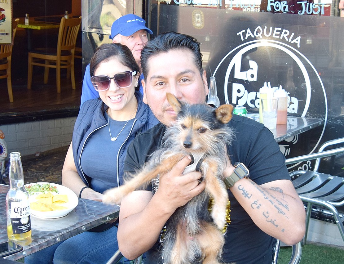 Lesley Daza (left) and her husband Orlando of Poningo Street find a comfortable spot in the outdoor seating area of Taqueria La Picardia to feast on snacks and drinks while enjoying the procession with their dog Koby.