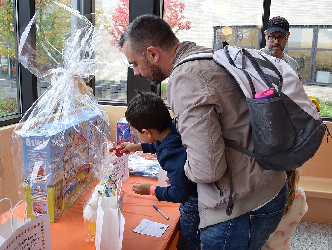 Martin Fernandez, a 4-year-old from Rye Brook, drops a raffle ticket into a bag to try his luck at winning a Bluey playset. His father Oscar gives him a lift.