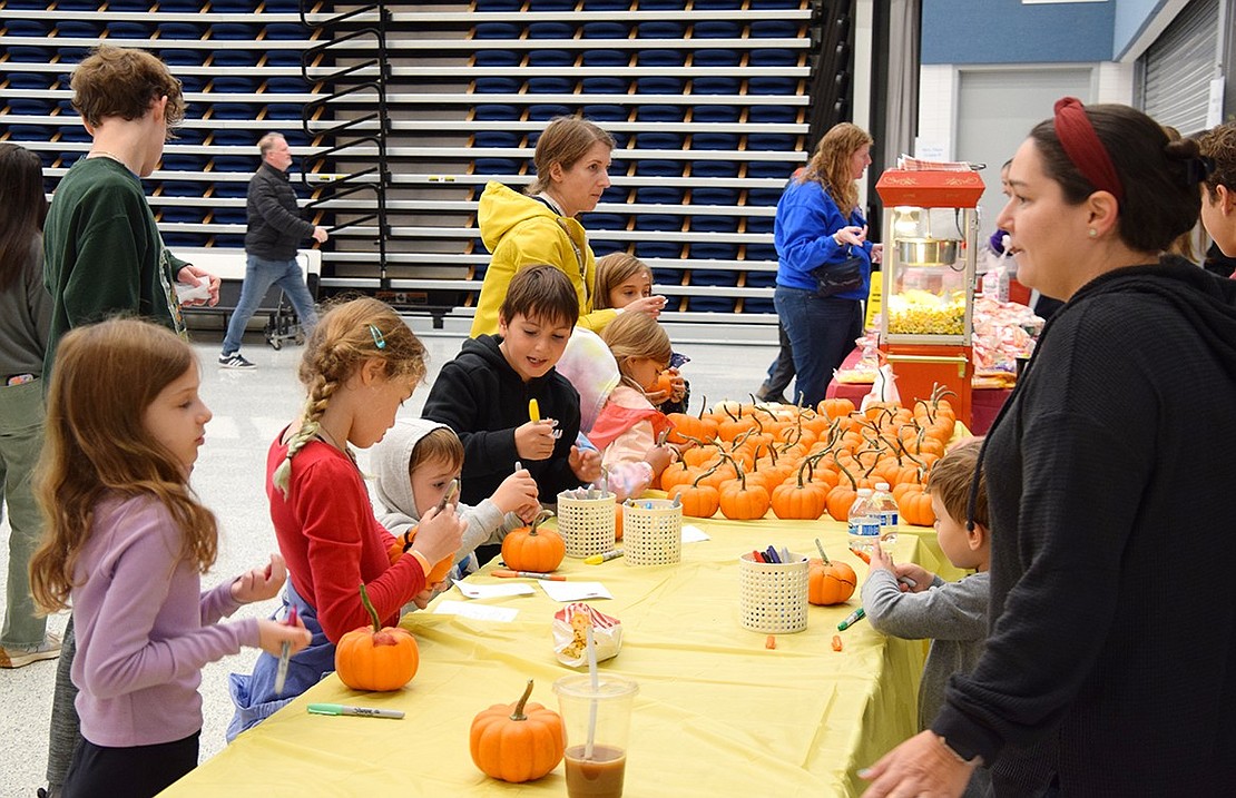 Kids of all ages spend time decorating small pumpkins with markers in the cafetorium.