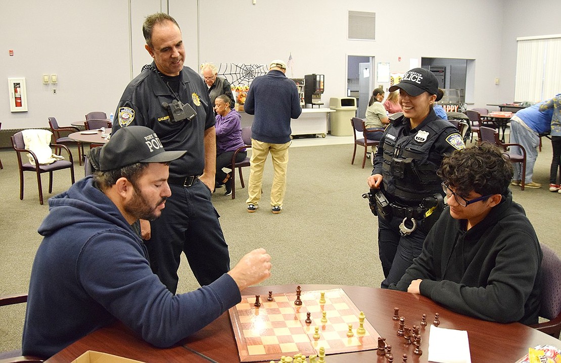 Port Chester Police Officer Joshua Perez (left) wraps up a game of chess against Port Chester Middle School student Steve Guardado as Lieutenant Robert Salerno and Officer Leslie Gutelius watch. Guardado would go on to win the game.