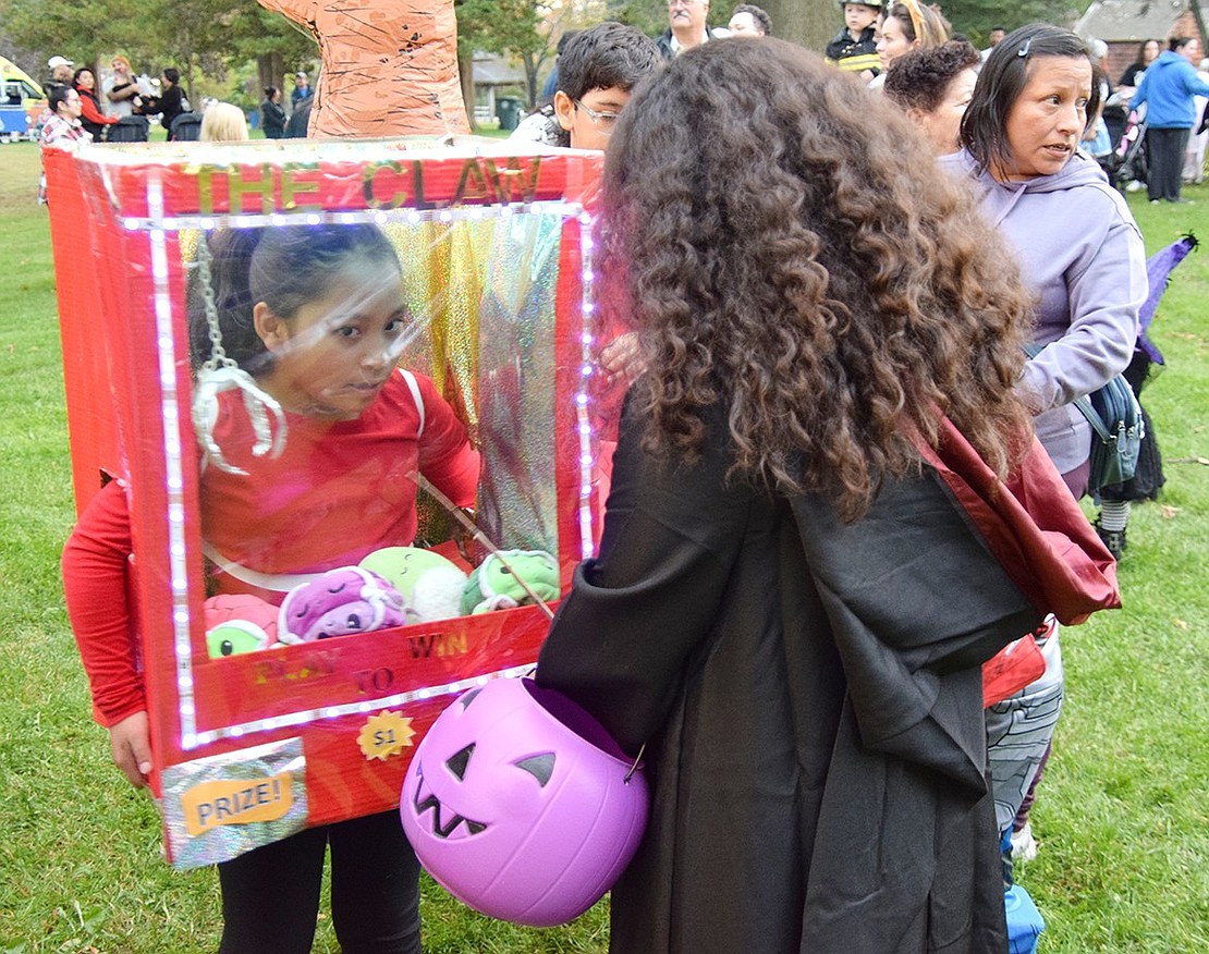 Eight-year-old Mia Carranza, a third-grader at Park Avenue Elementary School, shows other children some of the prizes in her claw machine costume.