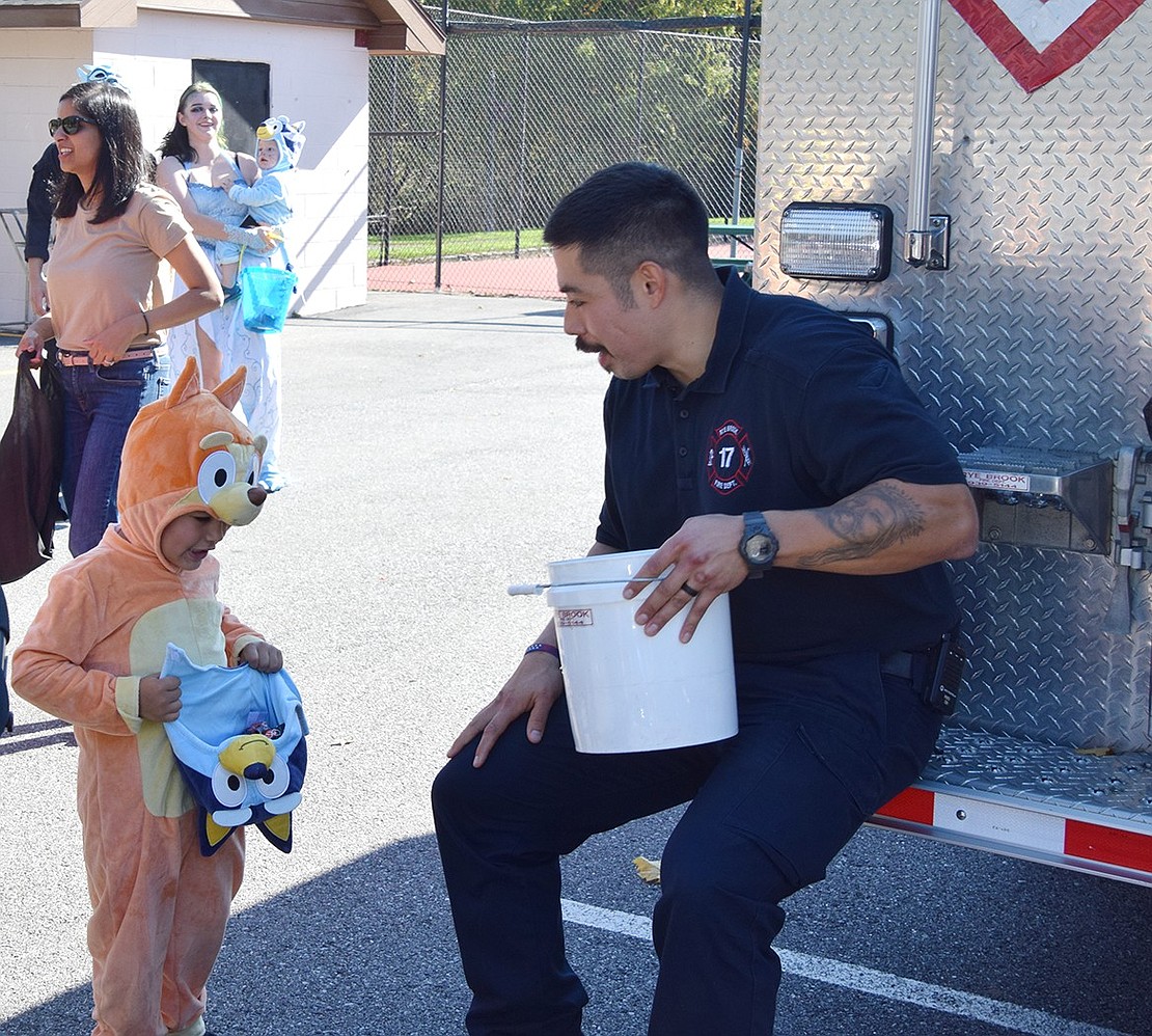 Carlos Ruano, a Rye Brook firefighter, hands out candy to 4-year-old Port Chester resident Omar Morfin, who is dressed as a dog from Bluey.