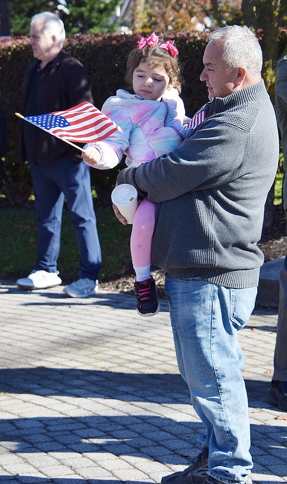 Four-year-old Emma Castellanos, held by her grandfather Ruben Alzate, waves the American flag at the ceremony. They live on Upland Street.