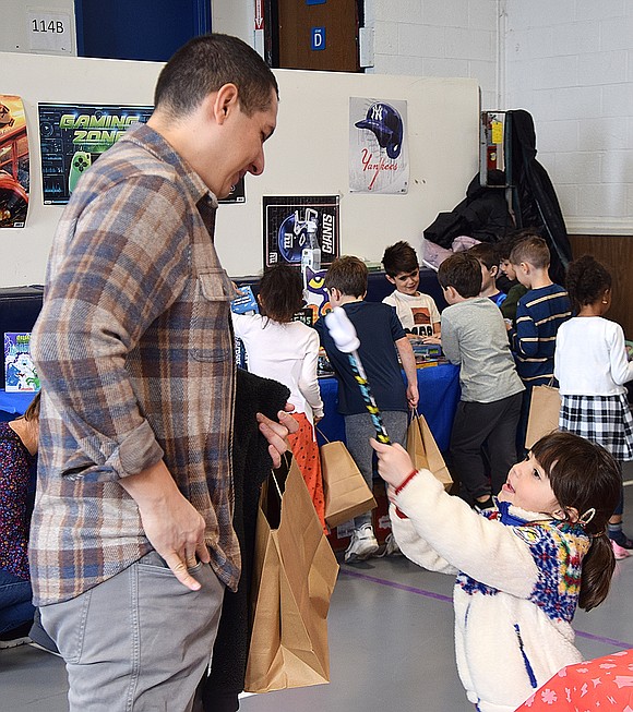 Annabelle Miranda, a kindergartener, pokes fun at her dad Alfred at the Ridge Street School Scholastic Book Fair, an annual PTA-sponsored pop-up event. This group of students, from the kindergarten and first grade classes, visited the old gymnasium at the school on Wednesday, Nov. 29, making purchases at the shop that will continue to host hours through Saturday.