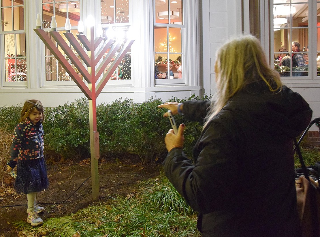 Crossway resident Debby Yablow directs 5-year-old Talia Szoke, who lives on Brush Hollow Close, to put her in position for the perfect picture under the menorah outside the Crawford Mansion Community Center.