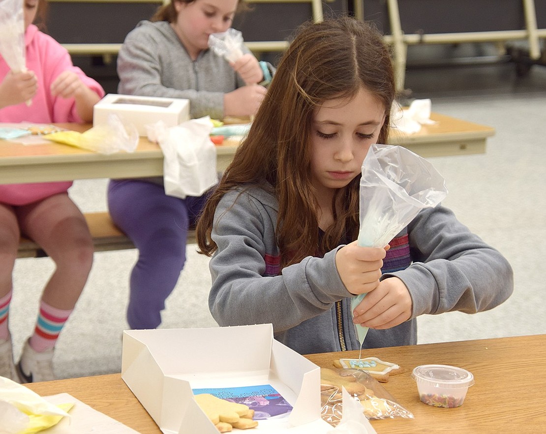 Slow and steady, and with strict focus, Ridge Street Elementary School fourth-grader Reese Wolf drizzles blue frosting onto a baked good in front of her in her school’s cafetorium on Wednesday, Dec. 13. She’s one of around 40 pupils enjoying the holidays with a cookie decorating night hosted by the Blind Brook PTA.