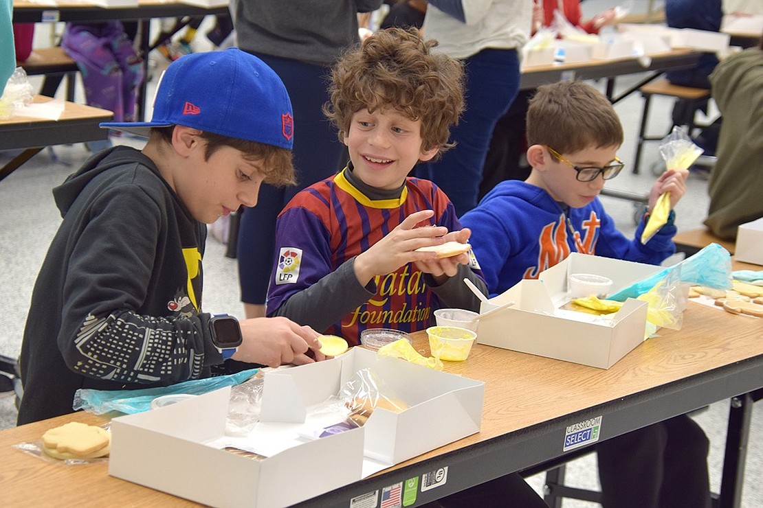 Fourth-graders John Gasparini (left), Alan Waisburg and Jake Klausman have some nice chatter and sing goofy songs as they spread frosting across all the baked goods in their kit. The cookies and decorating instructions were provided by Nora’s Ovenworks, a bakery based in Stamford, Conn.