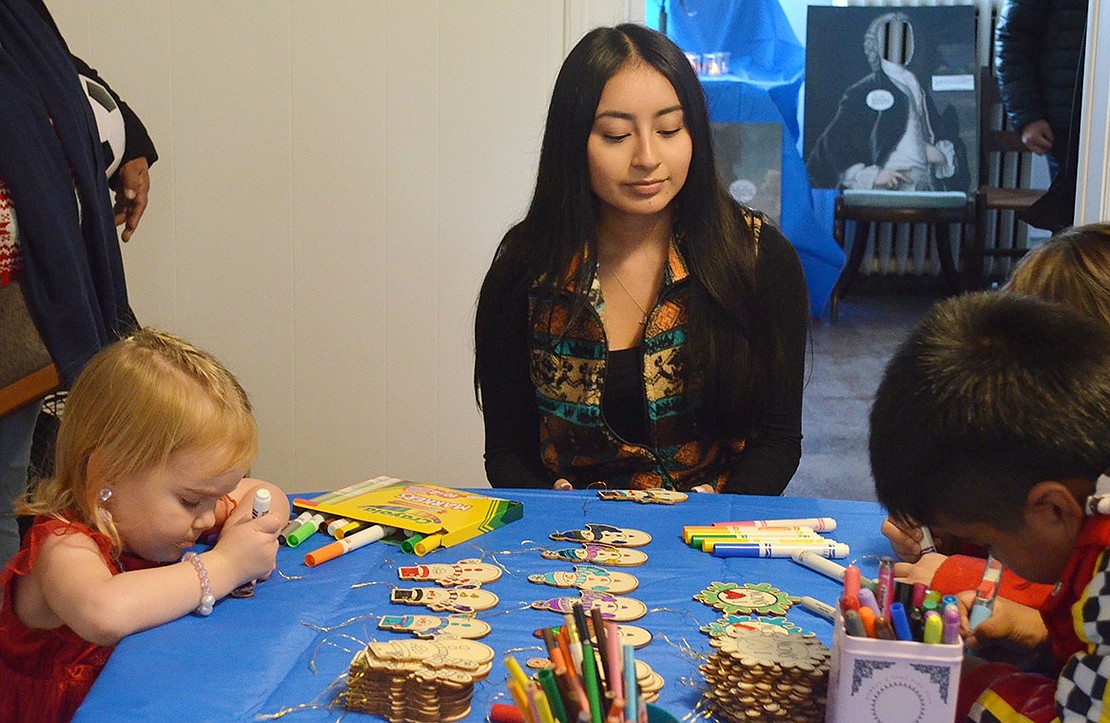 Port Chester High School junior and National Honor Society volunteer Kally Vichco oversees the craft table where 3-year-old Maggie Hartnett of Barrett Lane (left) and other children decorate ornaments.