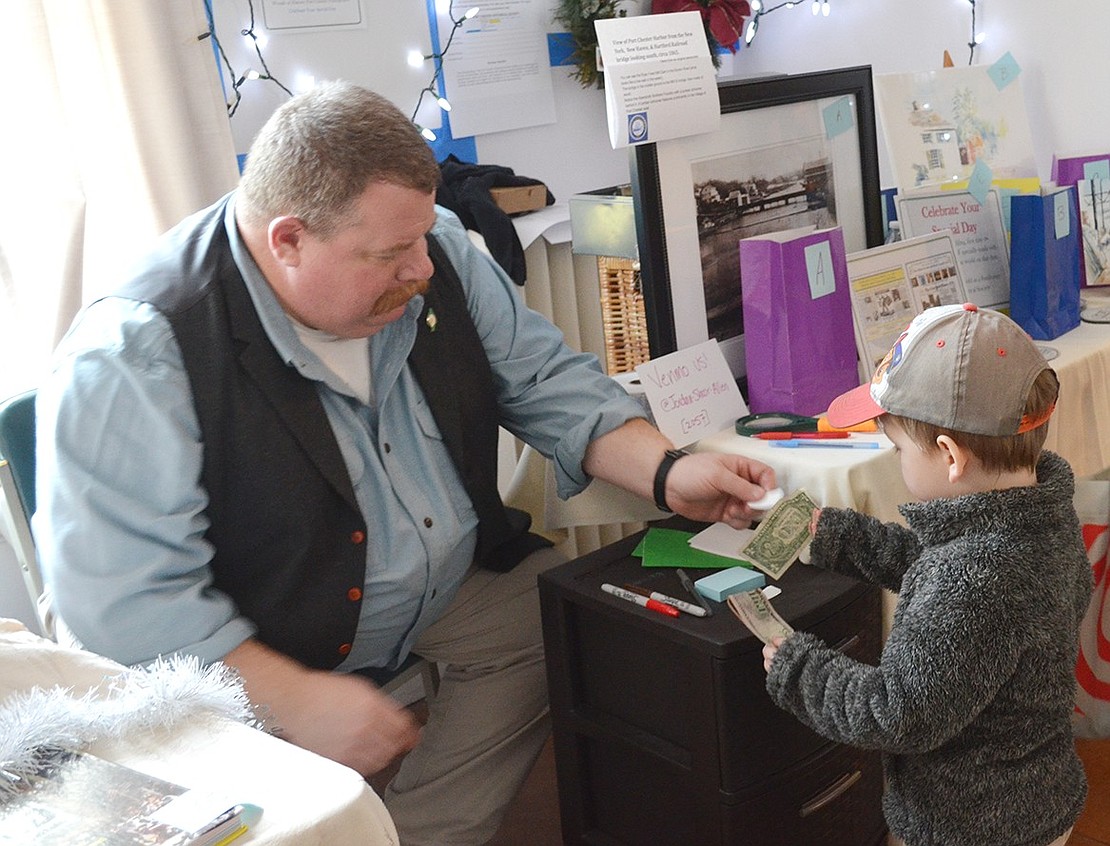 Theo Decker, 3, of Linden Street buys raffle tickets from Port Chester Historical Society board member Mike DeVittorio. There were many $1 raffle gifts as well as a table, at right, of more valuable $5 items with historic and/or Port Chester themes.