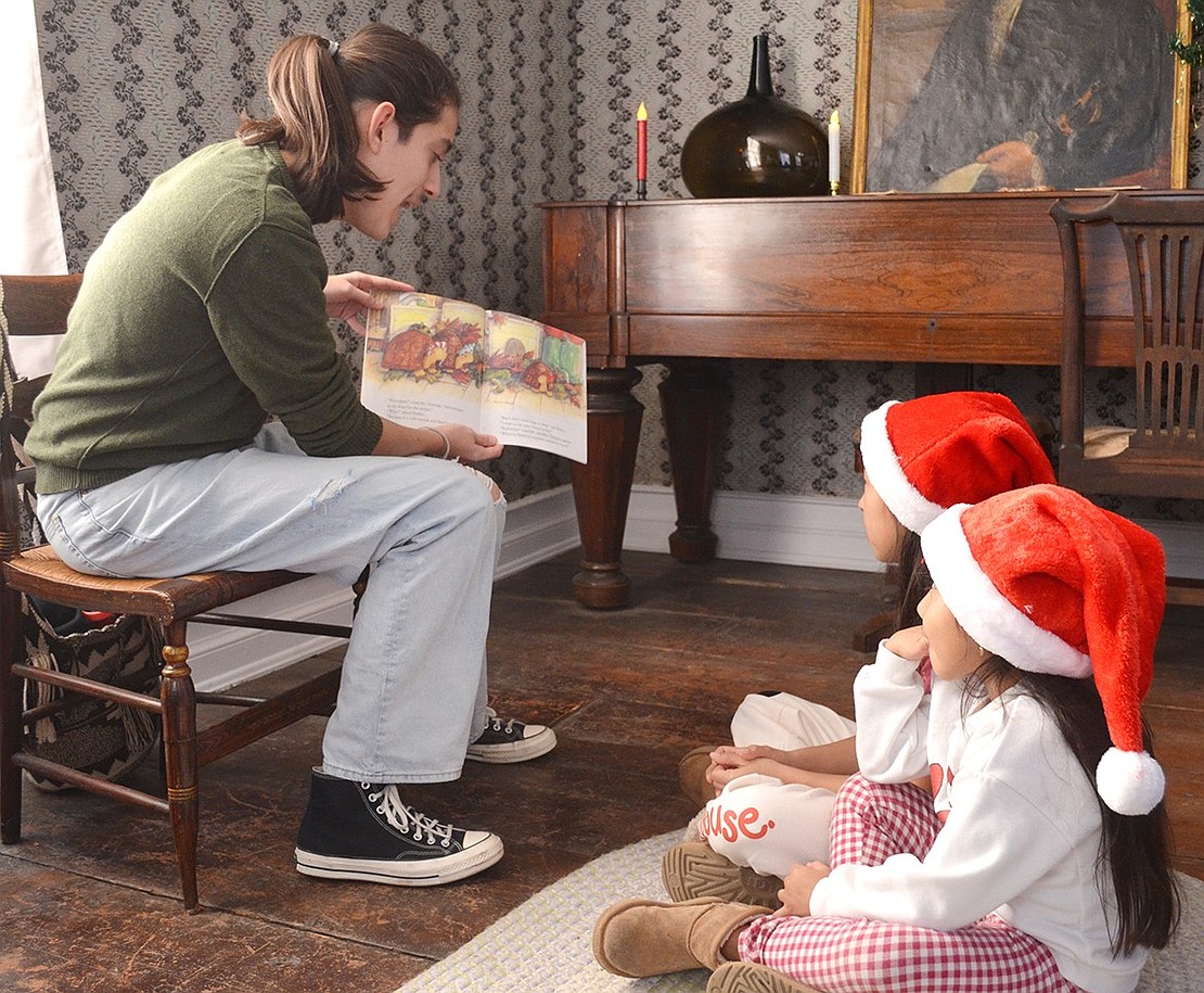 Sebastian Gimenez, a senior at Port Chester High School volunteering as a member of the National Honor Society, reads a holiday story to sisters Aliyah, 9, and Amaya, 5, Orozco of Highland Street at the Port Chester Historical Society’s Winterfest at the Bush-Lyon Homestead in Lyon Park on Saturday, Dec. 9.