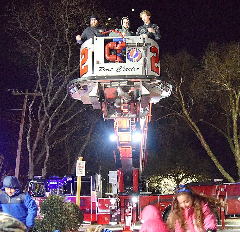 Port Chester volunteer firefighters Matt Ganz (left), Brian Benjamin and Julian Silva toss chocolate coins from their perch atop an engine ladder high in the air as children scramble to gather them at Port Chester’s first Chanukkah Gelt Drop on Thursday, Dec. 14. Outside of Village Hall, families gathered on the chilly evening for the event which featured live music and snacks.