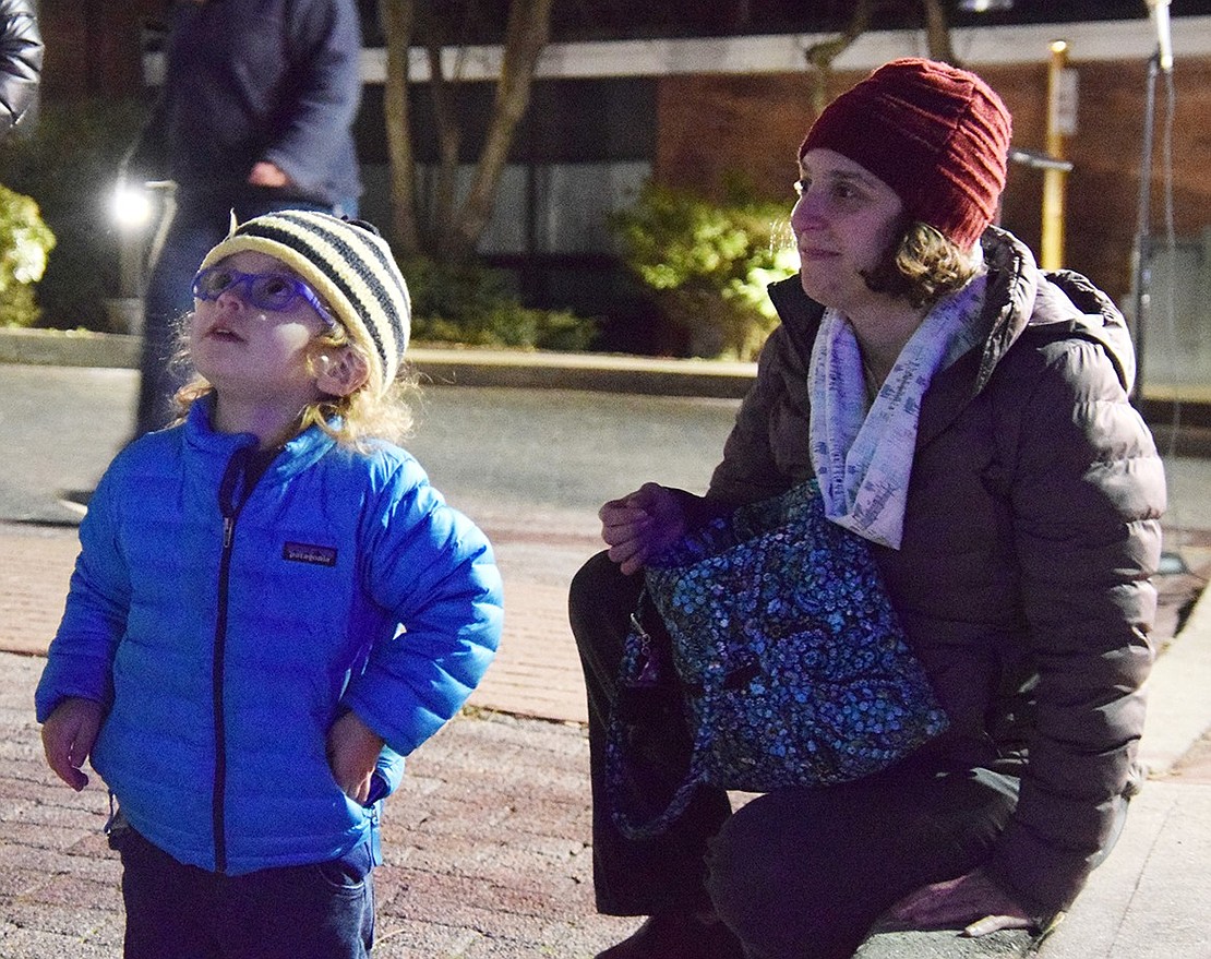 Nathaniel Butkiewicz, 3, looks up at the firefighters who are tossing candy down while his mom, Marissa Torento Butkiewicz, watches over him. The Port Chester resident has his pockets stuffed with chocolates.