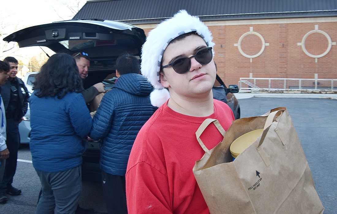 Wearing a festive Christmas hat, Port Chester High School senior Joshua Meyers carries a bag of donated food to a waiting truck on Dec. 21 as part of the food drive students organized to benefit the Don Bosco Community Center.