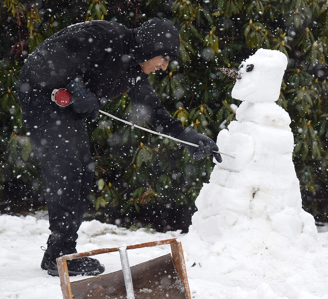 Sixteen-year-old Eduardo Xixitle puts the finishing touches on the unique snowman he and his siblings Leo, 14, Emmanuel, 16, and Itzayana, 7, created in their front yard at 391 Irving Ave. following the first snowfall of the season Saturday night, Jan. 6, which dropped 2-3 inches of snow in the Villages of Port Chester and Rye Brook. Snow continues to swirl the next day as Eduardo etches character into the body of their snow figure.