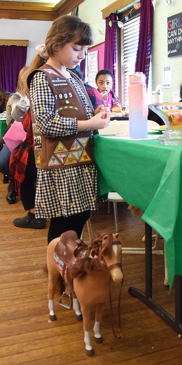 Port Chester resident Sophia Labrusciano, an 8-year-old member of Girl Scout Troop 1905, works on a friendship bracelet while her toy horse Cocoa stands at her feet.