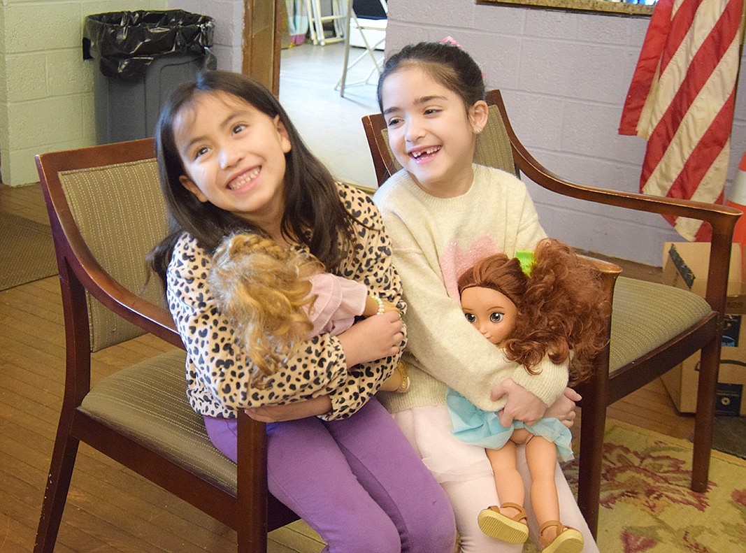 Seven-year-olds Nina Barrenechea (left) and Heidi Carniero share a chair, and a laugh, while waiting for a game of bingo to start. In the lap of the Port Chester residents are their dolls Alina and Emily, respectively.