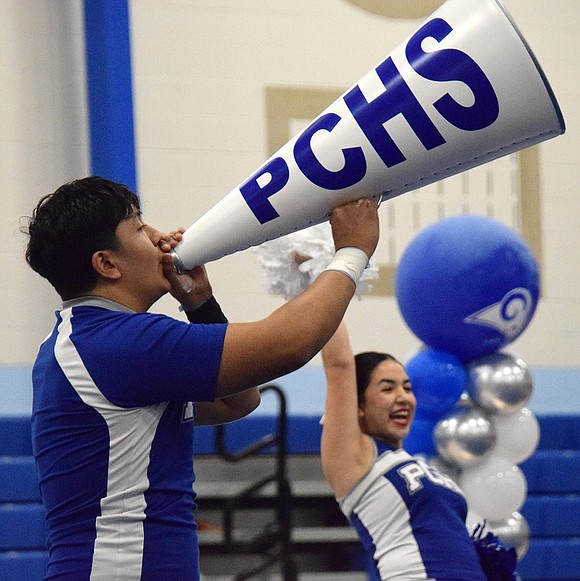 Senior Christian Flores yells into a megaphone, urging the crowd to make some noise for the Rams. To the right, junior Myisha Cruzi shows off her smile during the varsity team’s routine.