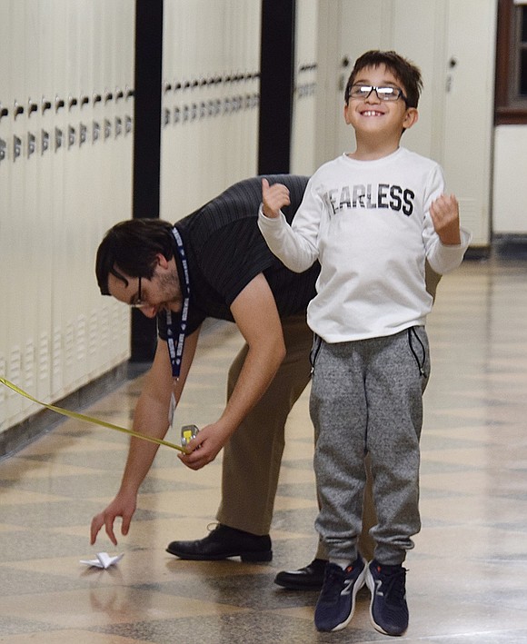 A master paper airplane maker, John F. Kennedy Elementary School third-grader Dylan Torres jumps for joy as high school math teacher Anthony Perciavalle measures his craft’s flight distance and announces a record-breaking 426 inches.