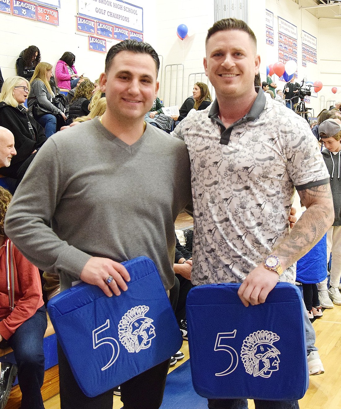 Steve Gross (left) and Chris Stockel pose for a photo with their 50-year-anniversary gift from the Friends of Blind Brook in the high school gym on Friday, Feb. 9. The two are alumni of Blind Brook High School who played on the state championship-winning boys’ varsity basketball team in 2004. They, alongside the 2002 state champs and both boys’ and girls’ 1976 inaugural teams, were recognized for their impact on the Blind Brook community.