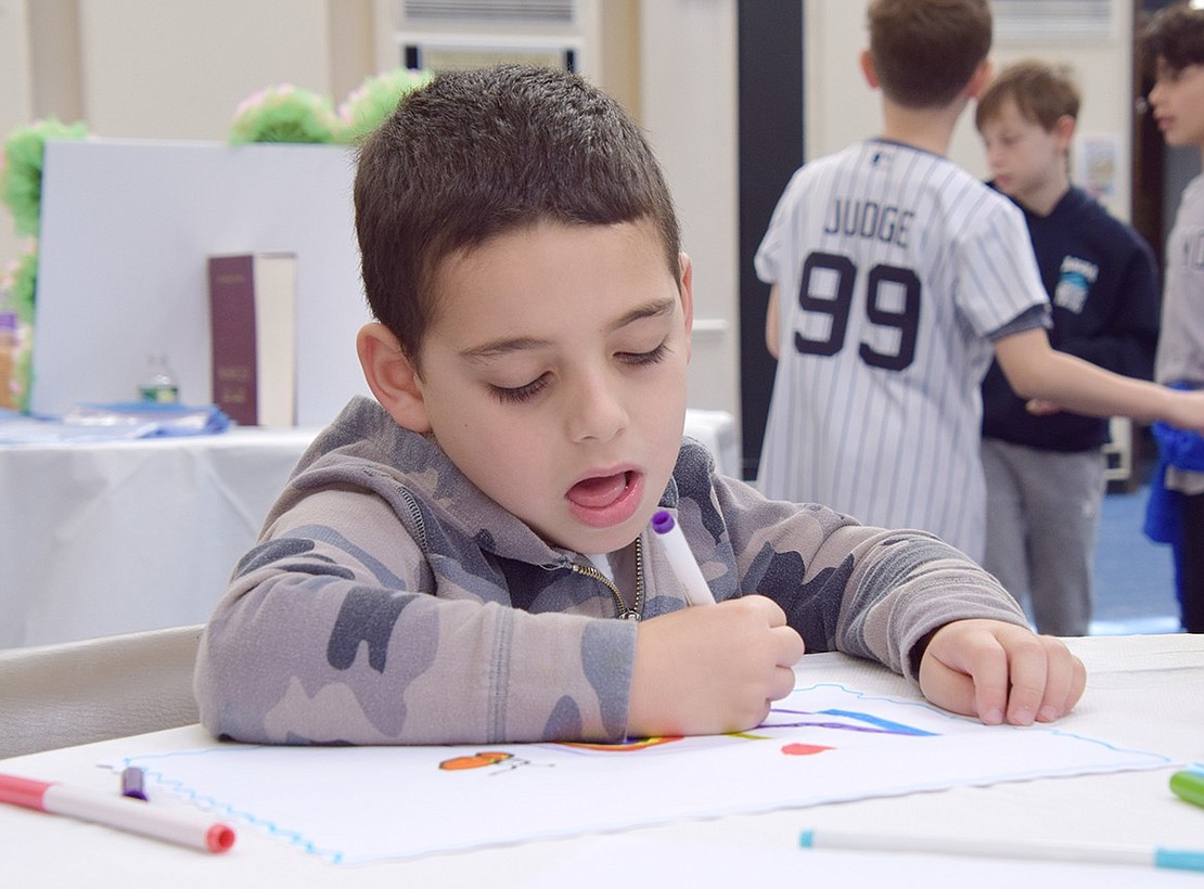 With a face showing his focus, Ridge Street School kindergartner Nolan Schleifer, 5, designs a placemat at one of the tables set up for activities. The drawings will be donated to King Street Rehab.