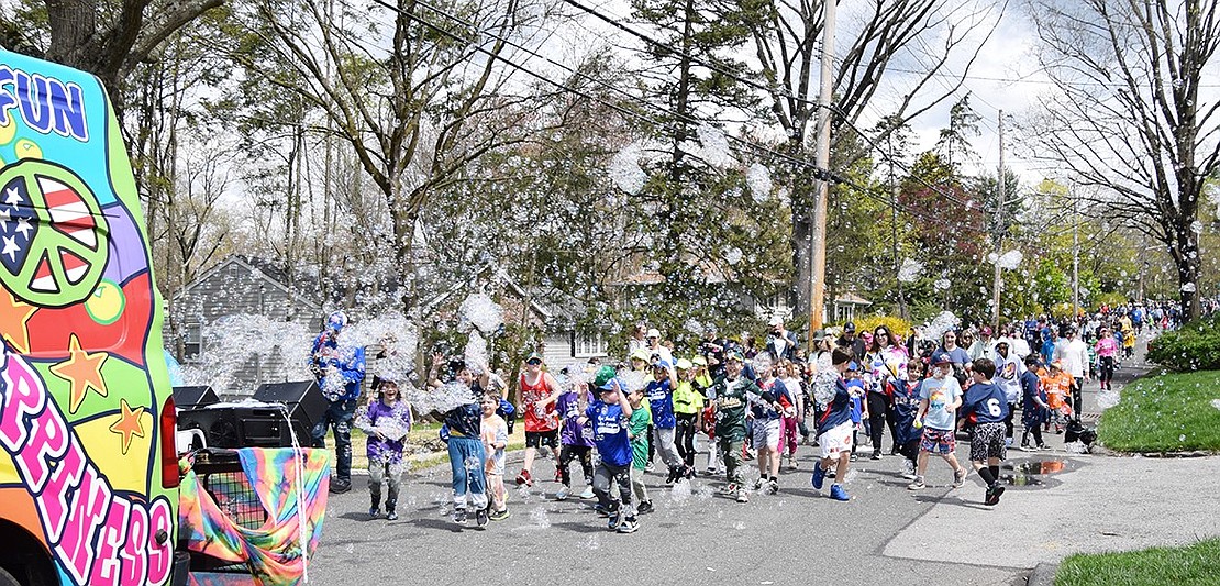 Hundreds of Rye Brook Little League family members make their way to Pine Ridge Park, playing with bubbles from the bus that led them during their march down Windingwood Road.