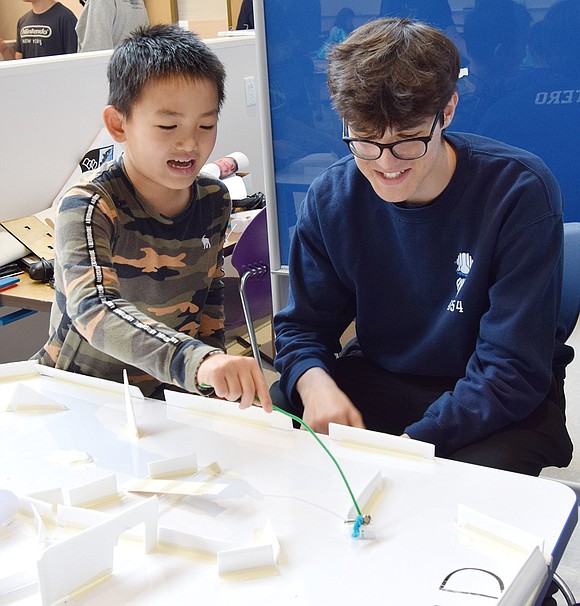 Fourth-grader Jason Zhou animatedly guides his BristleBot through a maze as Blind Brook High School robotics club president Joaquin Otero laughs.