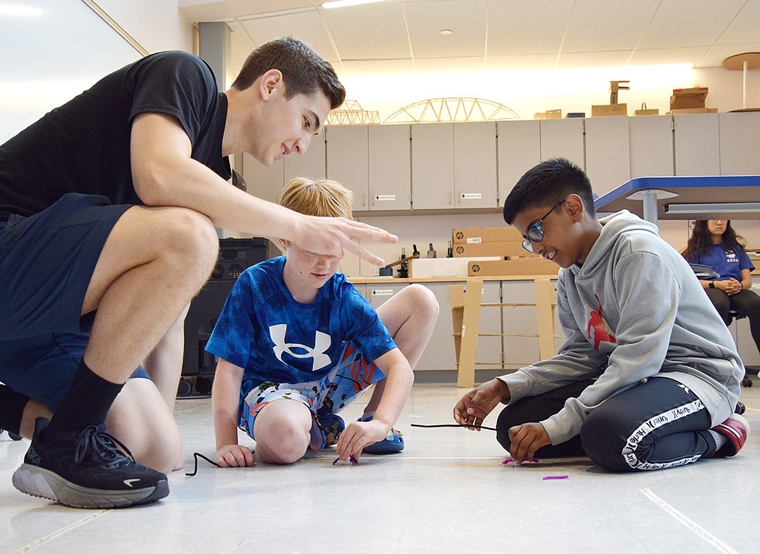 Max Harvey (left), a sophomore volunteer at the event, begins a countdown for fifth-graders Connor Ware and Gabe John to race their robots on the floor of the Fab Lab.