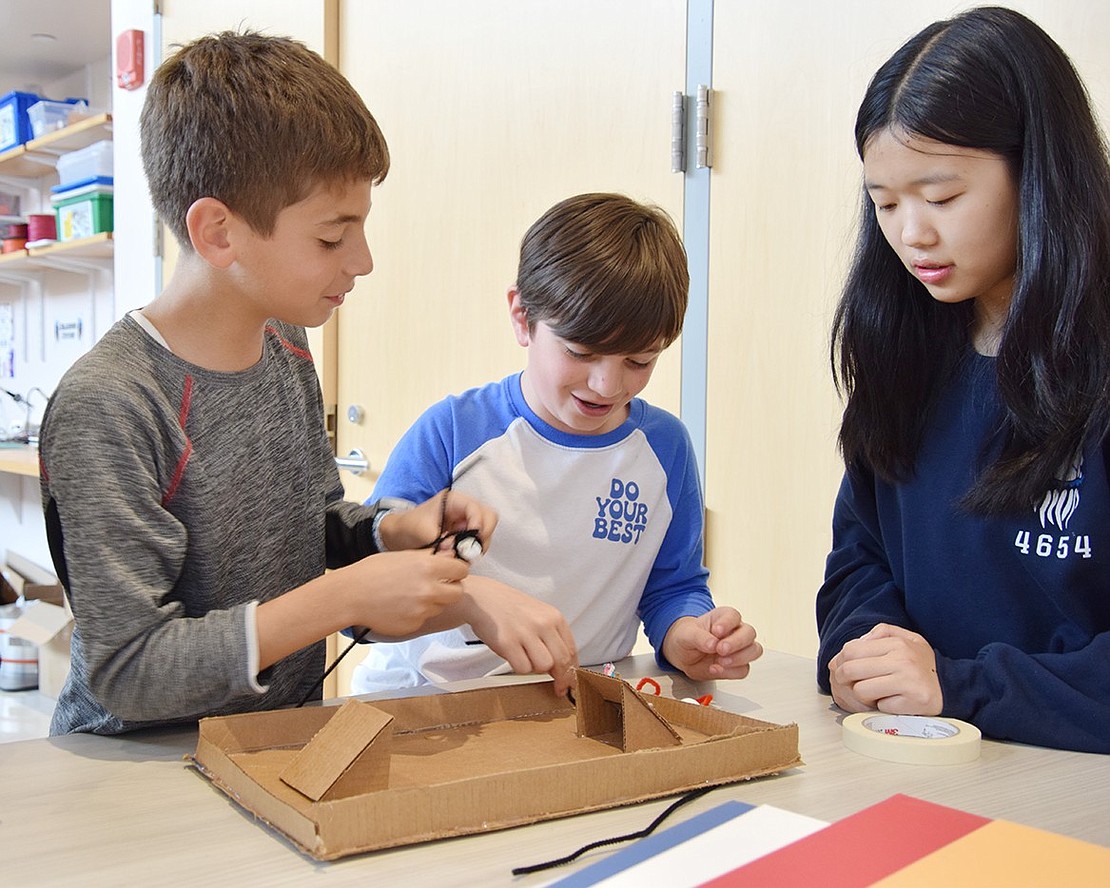 Fifth-graders Anthony Gebrael (left) and M.J. O’Neill pit their BristleBots against each other in a mini-soccer game while freshman robotics club member Iris Chen acts as referee.