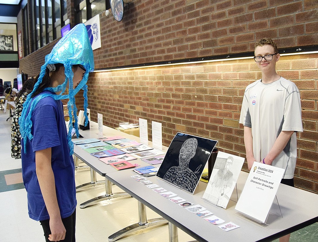 Though Blind Brook High School sophomore Abigail Weintraub (left) is in attendance as part of the robotics club, she still takes time to admire other students’ works, like junior Luke Ross’s self portraits and character drawings.