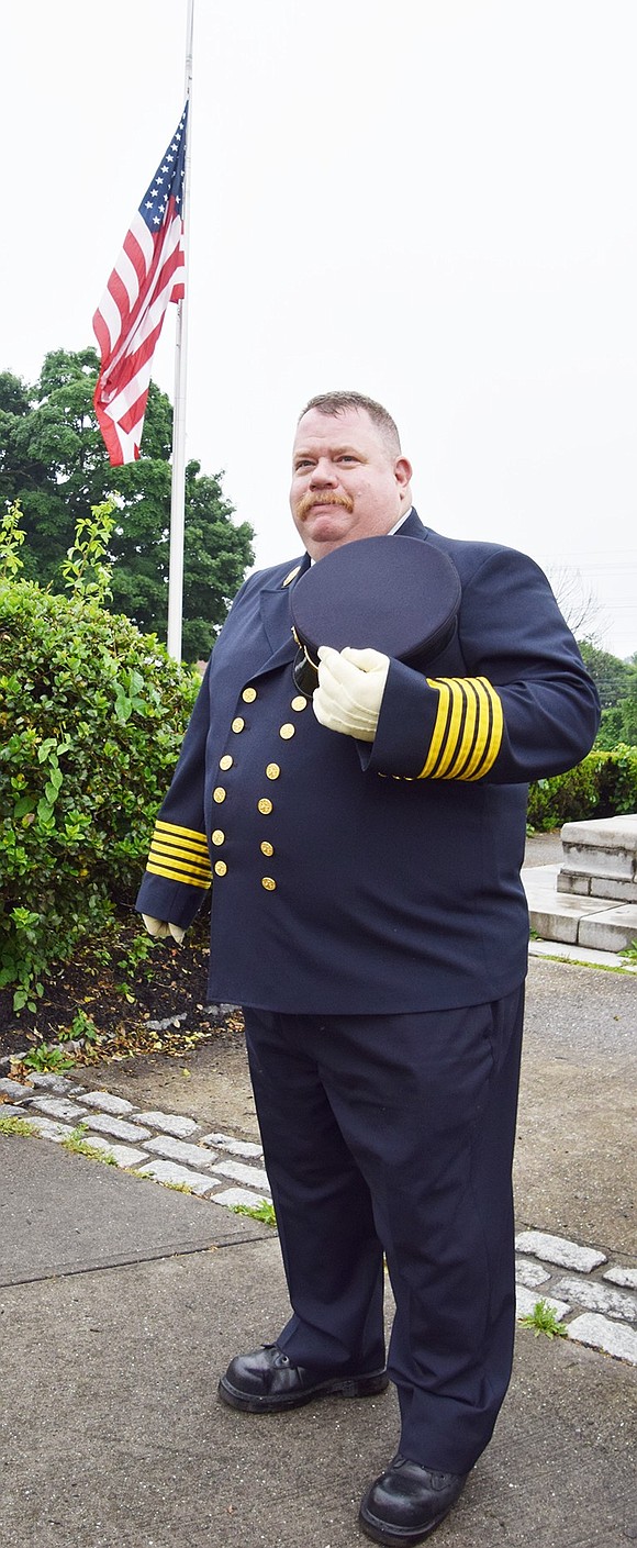 Former Port Chester Fire Chief Michael DeVittorio speaks about the history of the Civil War monument at the corner of New Broad and Pearl streets, where the large American flag, flying at half staff, flutters in the wind.