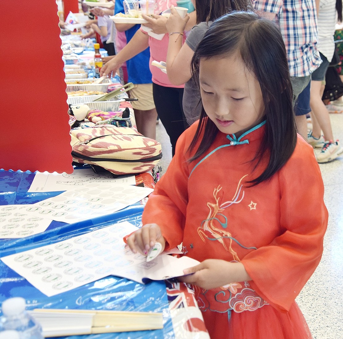 Six-year-old kindergartner Emily Liu dons a Chinese dress while collecting stickers for her passport at the South Korea table.