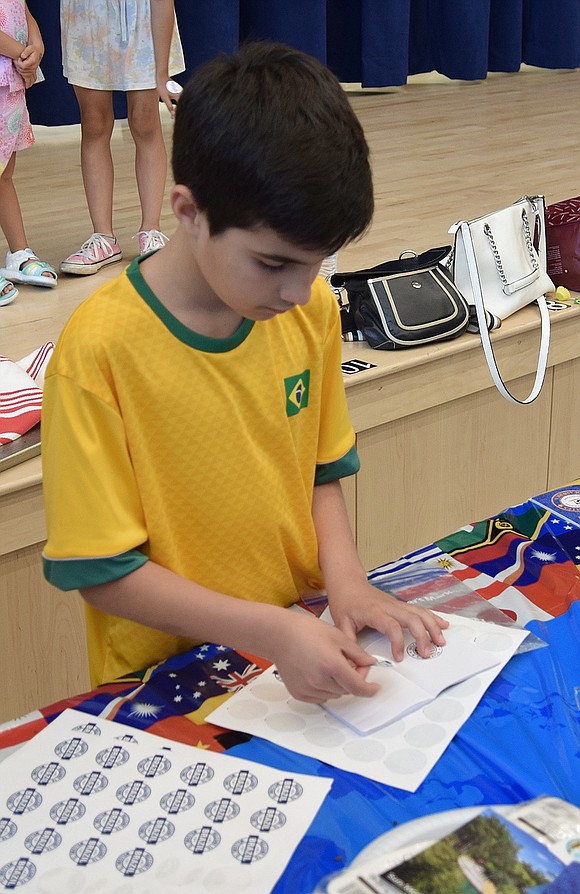 Third-grader Lucca Pinheiro Jany helps at the Brazil table by placing stickers in visitors’ passports.