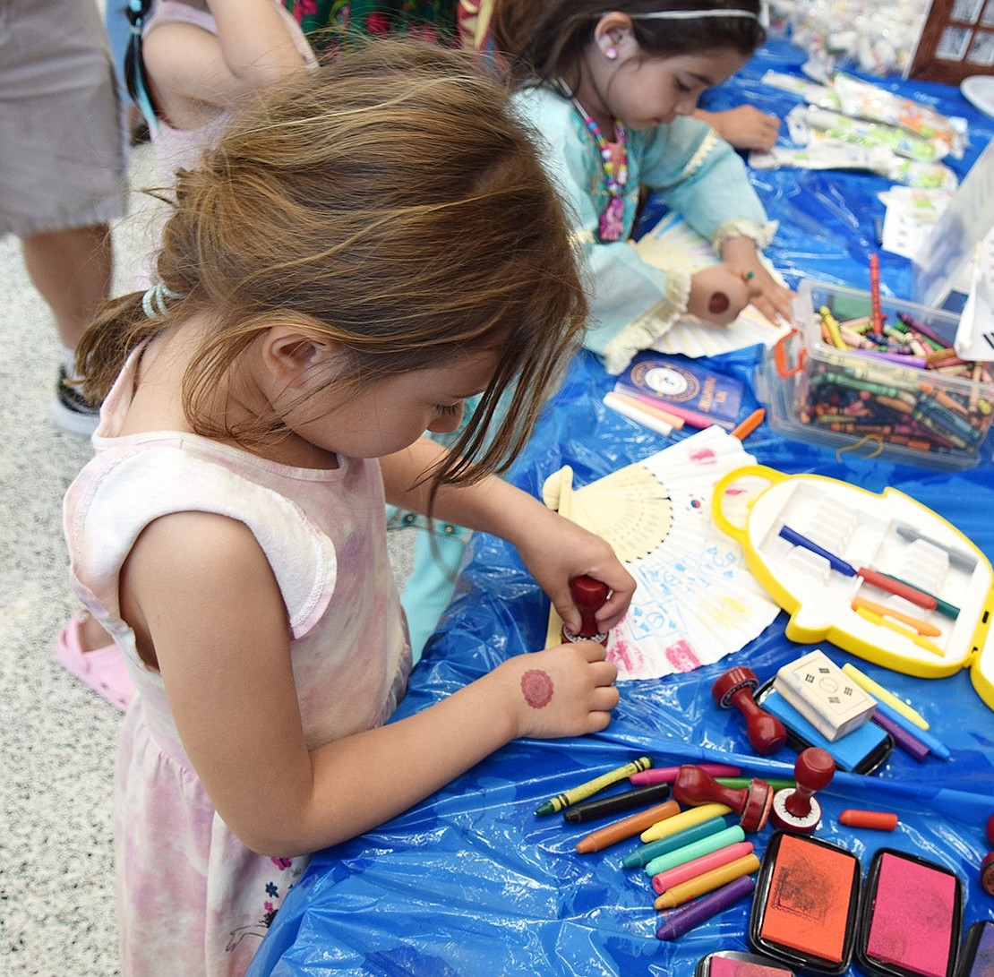 Kate Brzov, a 5-year-old kindergartner, applies colorful stamps to a fan as an arts and crafts activity at the South Korea display.