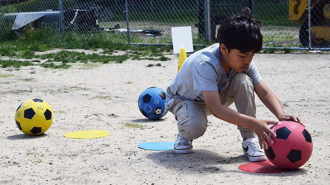 In the quiet moments before the race kicks off, third-grader Jacob Martinez helps set up soccer balls that each competitor will need to score into a goal to advance.