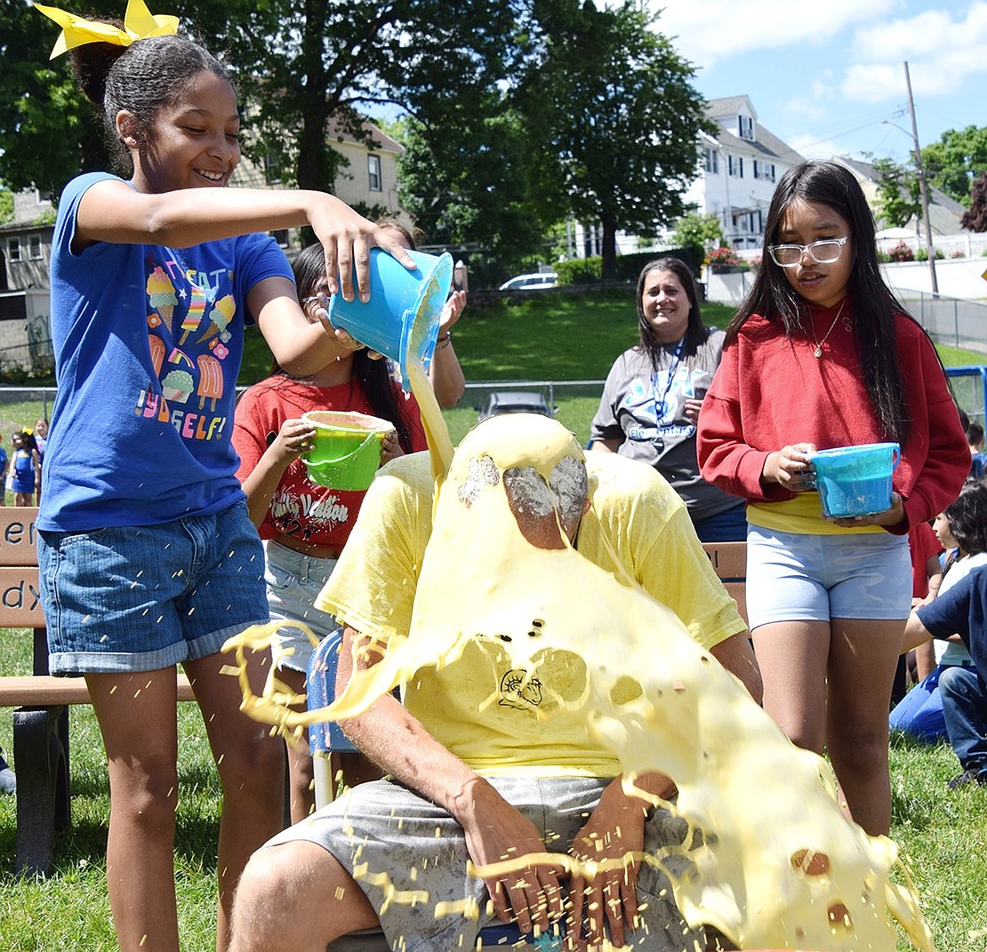 Fifth-grader Lola Dulanto pours a bucket of yellow slime onto her teacher Rich Gregory at the John F. Kennedy Elementary School SLOPstacle Race on May 30. Held on the lower playground, the annual event saw teachers, staff and PTA members get the messiest students had ever seen.