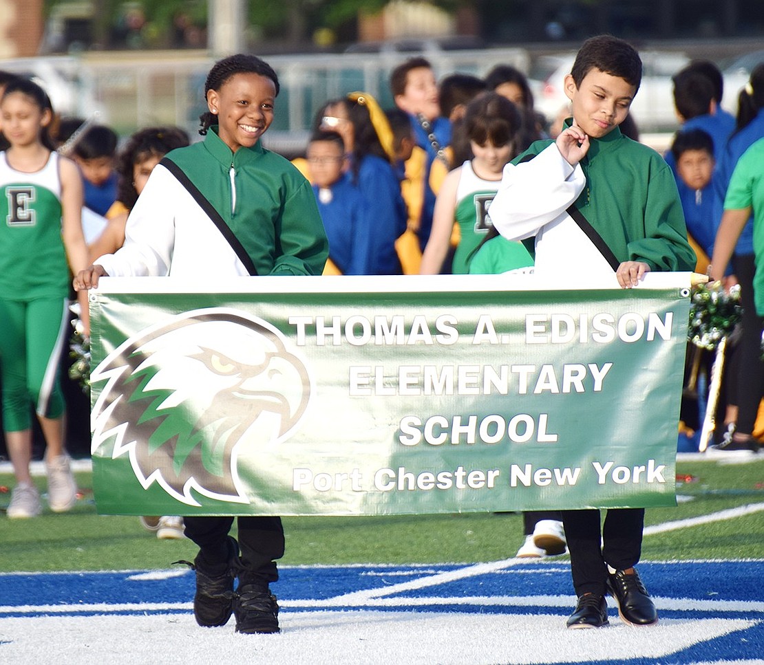 Edison School fifth-graders Carmelo Wilcox (left) and Joao Braz get their spirit squad’s show started with smiles by leading their school’s team onto the field with their banner.