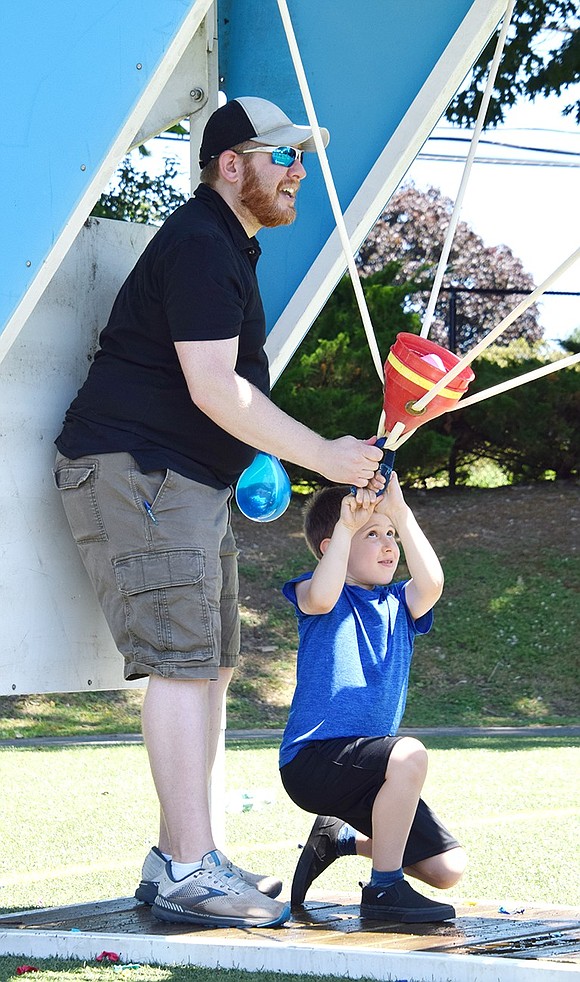 Rye Brook resident Kevin Heaps helps his 5-year-old son Abraham load and launch a water balloon in a battle station set up on the field.