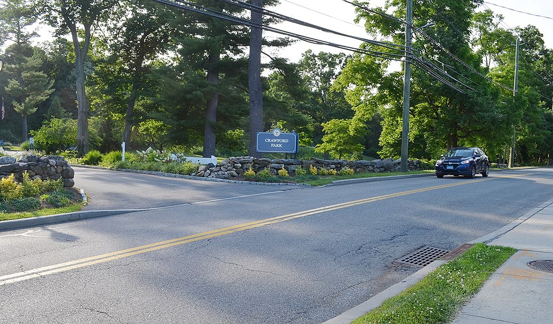 View looking across North Ridge Street toward the northern side of the Crawford Park driveway showing the stone wall that might have to be disturbed to create a pathway if a crosswalk were constructed to make for safer walking. It also shows the storm drain and wide driveway across the street from the driveway which must be avoided.