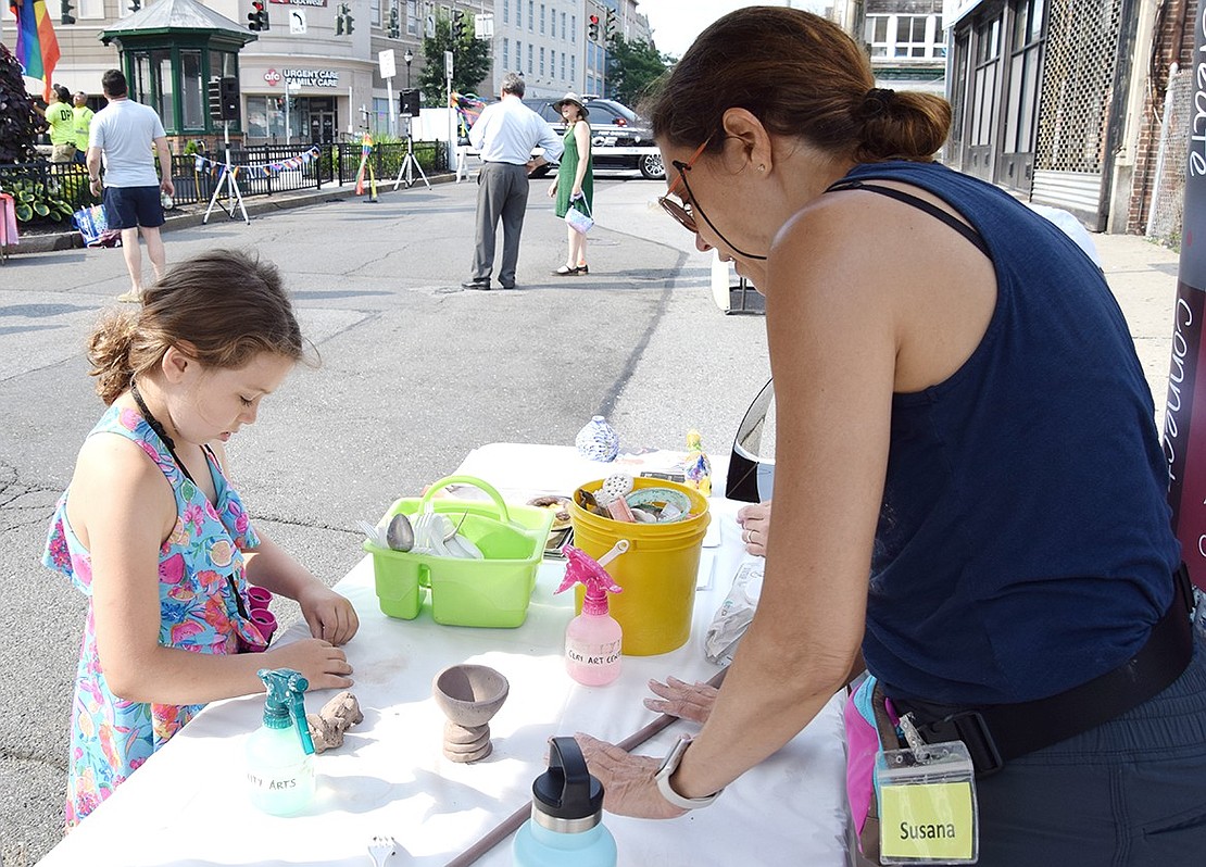 Ryan Allen, 7, starts the process of creating a clay cup as Suzana Valera, an art teacher from the Clay Art Center manning an activities table, offers advice.