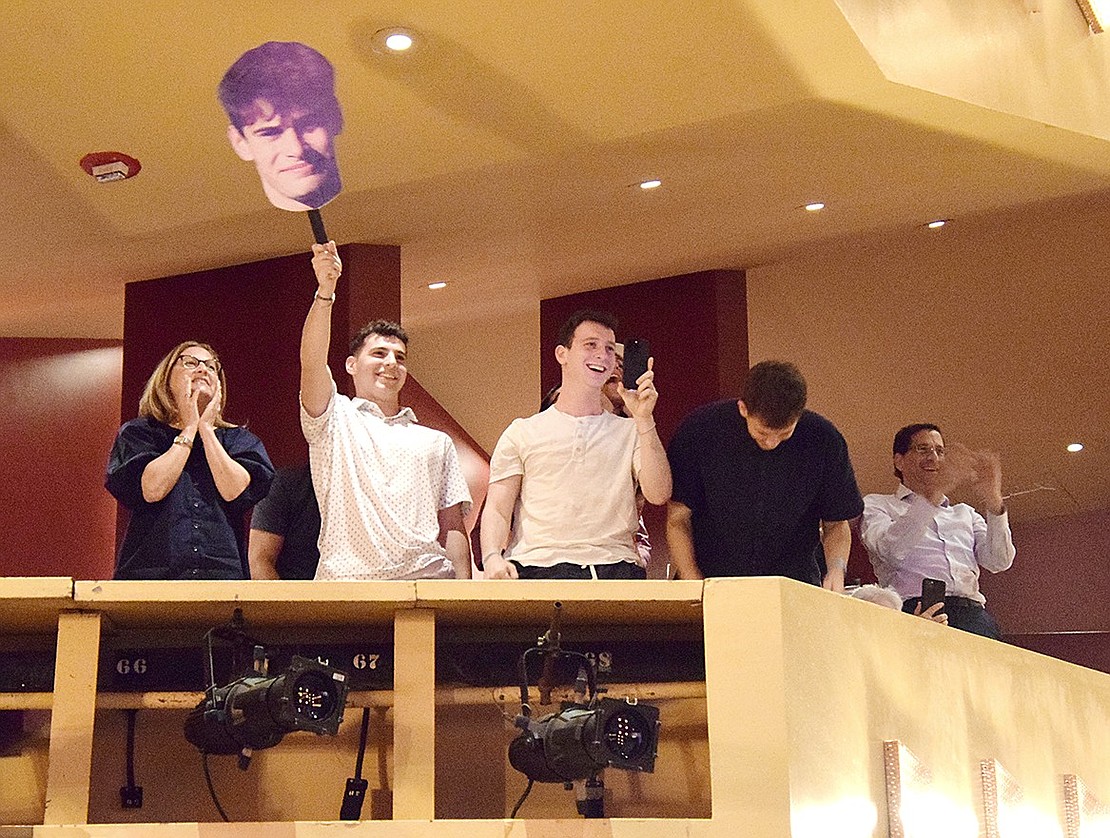 Family and friends of Eli Zimmerman go nuts when his name is called, cheering from the auditorium balcony and waving a cardboard cutout of his face.