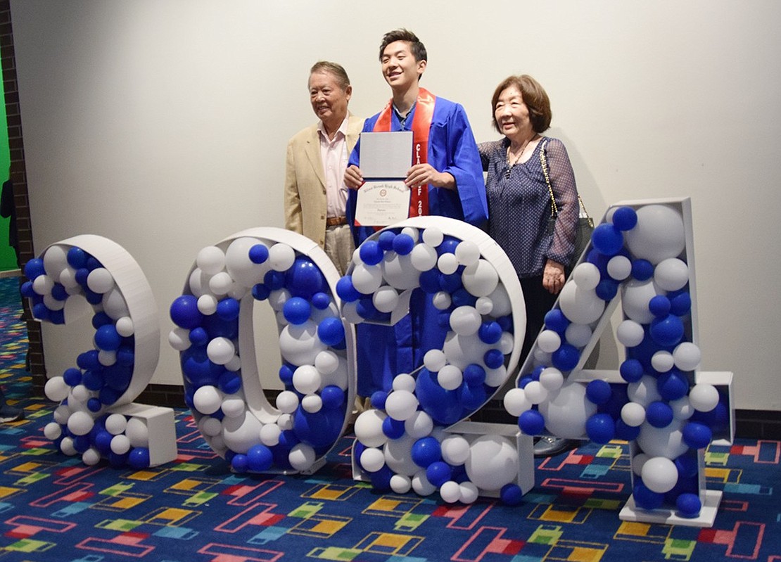 Posing for a photo by the Class of 2024 décor set up in the lobby, Takashi Kimura shares the special moment with his grandparents Yoshiaki and Mitsuko.