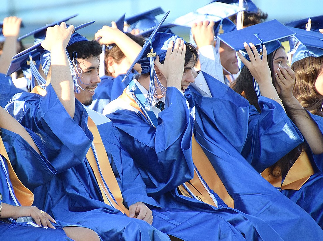 As a gust of wind tries to steal their caps, Anthony Enriquez (left), Thomas d’Esperies and Amanda DeFeo laugh as their valedictorian cracks a few jokes during his speech at the Port Chester High School graduation ceremony on June 27.