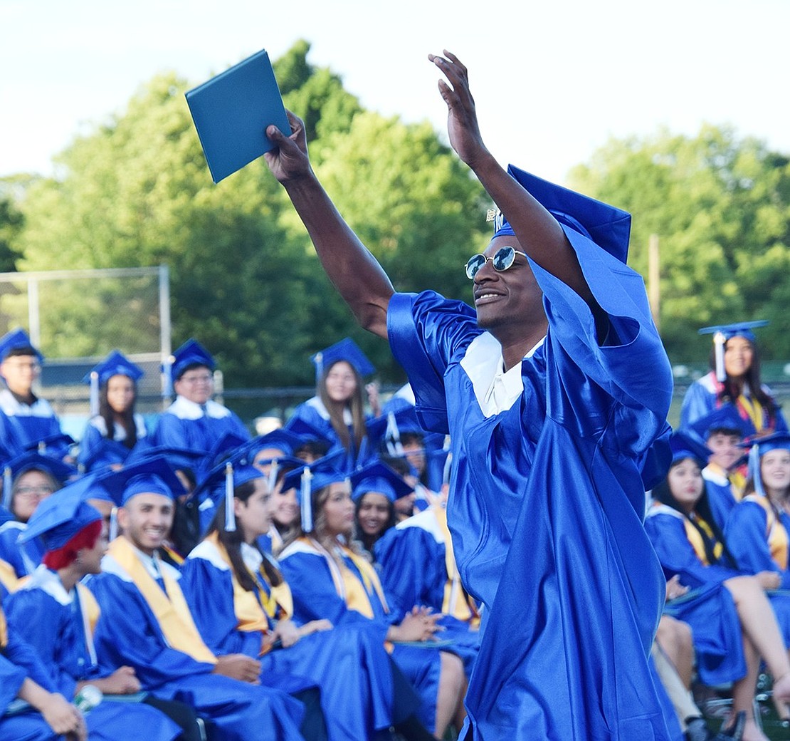 Finally done! Ronald Harris proudly holds up his diploma and motions toward his family, who found a front-row spot to watch him graduate.