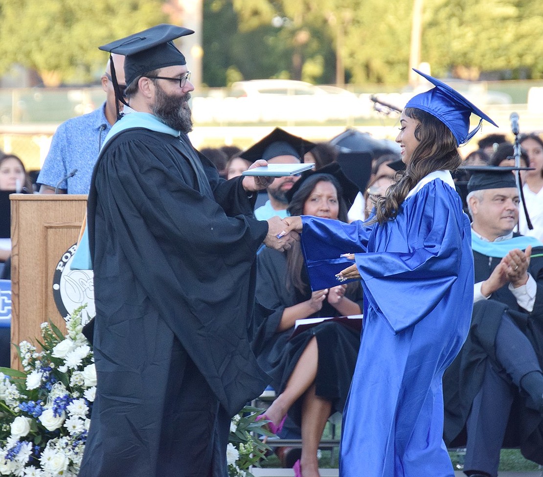 Board of Education member Rob Dominguez shakes hands with Dachesca Payano Abreu to award her a diploma.