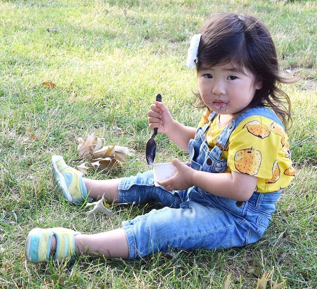 Rui Chiaki, a 4-year-old who recently moved to North Ridge Street from Tokyo, Japan, with her family, savors a frozen snack from her seat on the grass in Pine Ridge Park. She joins the dozens of others who stopped by the Village of Rye Brook’s Ice Cream Friday on July 5.