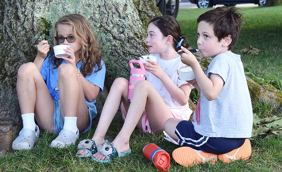 Rising Ridge Street School fourth-grader Gabi Ferdschneider (left) enjoys her cool treat while sitting under the shade of a tree alongside her friend Taylor Cirillo, 9, and younger brother Troy, 6.